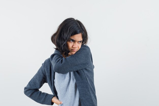 Jeune fille étirant une main comme tenant quelque chose et pointant vers elle avec l'index en t-shirt gris clair et sweat à capuche zippé gris foncé et à l'épuisé