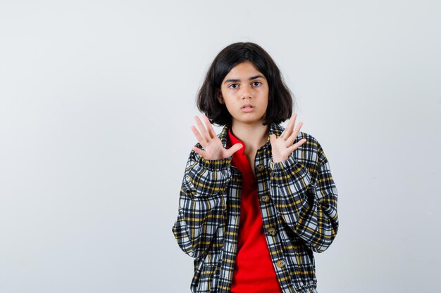 Jeune fille étirant les mains comme tenant quelque chose en chemise à carreaux et t-shirt rouge et l'air surpris. vue de face.