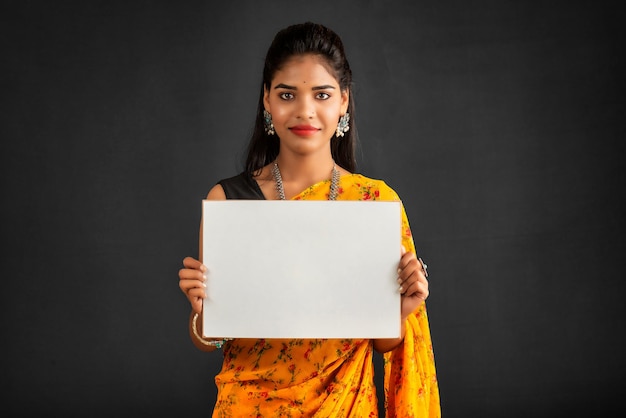 Une jeune fille ou une femme d'affaires portant un sari et tenant une pancarte dans ses mains sur un fond gris