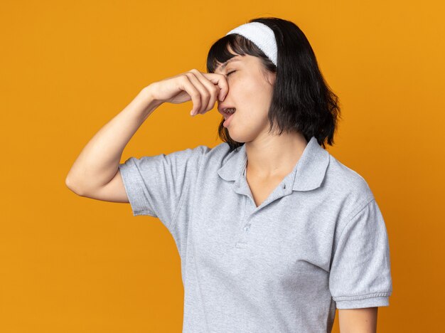 Jeune fille fitness portant un bandeau fermant son nez avec des doigts souffrant de puanteur debout sur orange