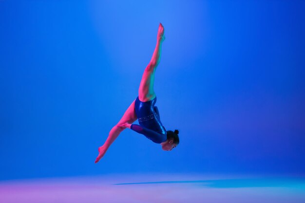 Jeune fille flexible isolée sur fond de studio bleu Jeune modèle féminin pratiquant des exercices de gymnastique artistique pour l'équilibre de flexibilité