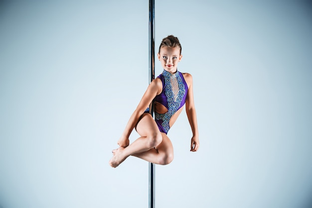 La jeune fille forte et gracieuse effectuant des exercices acrobatiques sur pylône