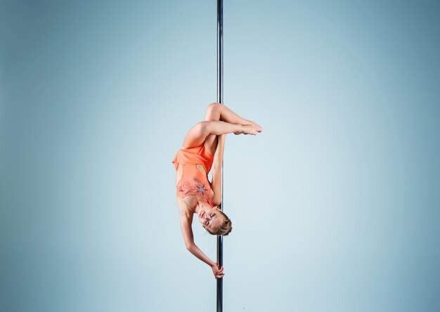 La jeune fille forte et gracieuse effectuant des exercices acrobatiques sur pylône