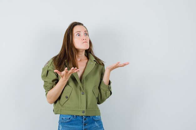 Jeune fille gardant les mains de manière interrogative en veste, short vue de face.