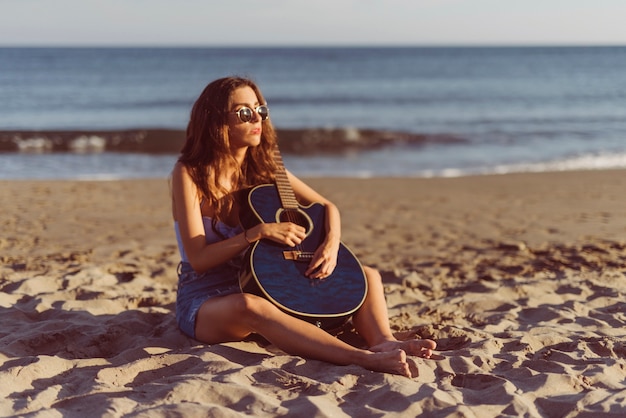Jeune fille avec une guitare assise sur le sable