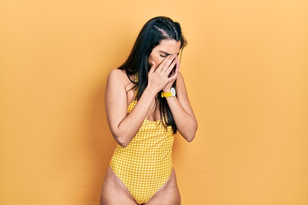 Jeune fille hispanique portant un maillot de bain avec une expression triste couvrant le visage avec les mains en pleurant. notion de dépression.