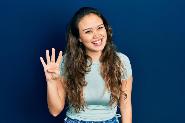 Jeune fille hispanique portant des vêtements décontractés montrant et pointant vers le haut avec les doigts numéro quatre tout en souriant confiant et heureux.