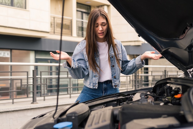 Une jeune fille inquiète utilise un téléphone pour expliquer au mécanicien le problème avec une voiture qu'elle a.