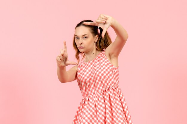 Jeune fille en jolie robe rose souriant et prenant une photo avec ses mains sur le rose