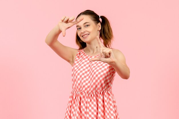 Jeune fille en jolie robe rose souriant et prenant une photo avec ses mains sur le rose