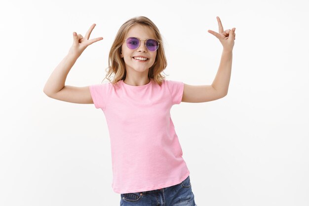 Une jeune fille joyeuse, élégante et glamour profite des vacances d'été sans école, porte des lunettes de soleil t-shirt rose