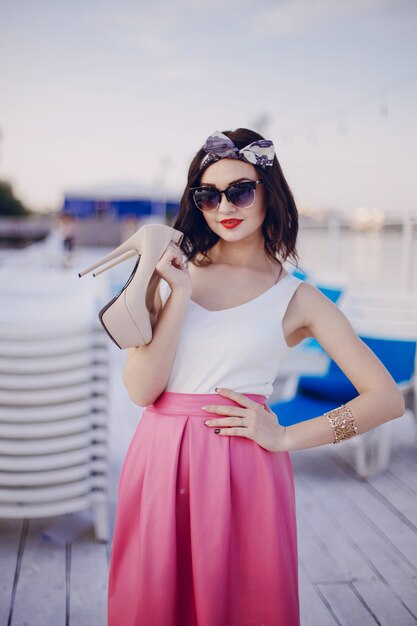 Jeune fille avec jupe rose posant avec des lunettes de soleil et hauts talons