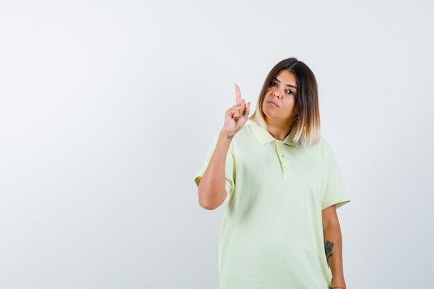 Jeune fille levant l'index en geste eureka en t-shirt et à la vue sensible, de face.