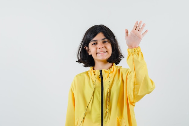 Photo gratuite jeune fille levant la main en saluant quelqu'un en blouson jaune et à la joie