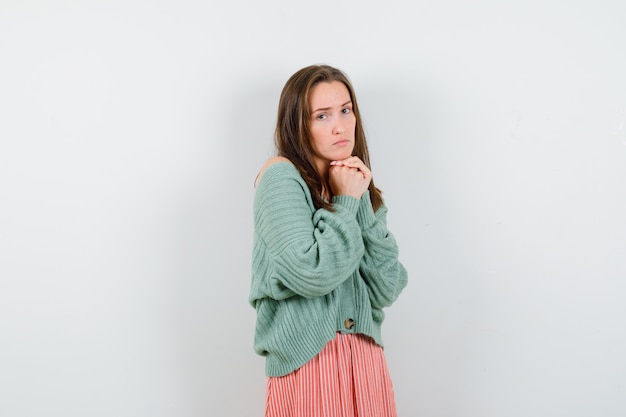 Jeune fille en maille, jupe joignant les mains en position de prière, regardant par-dessus l'épaule et regardant sérieusement, vue de face.