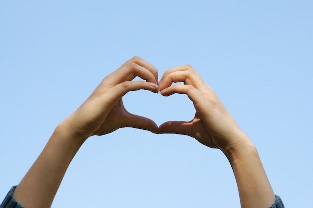 Jeune fille mains tenant la main en forme de coeur avec le fond de ciel bleu clair