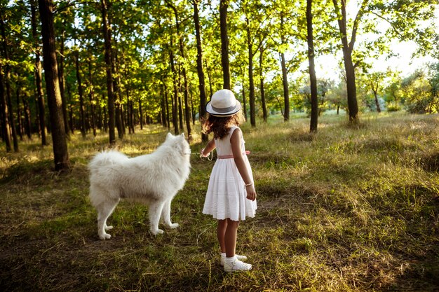 Jeune fille marchant, jouant avec un chien dans le parc au coucher du soleil.