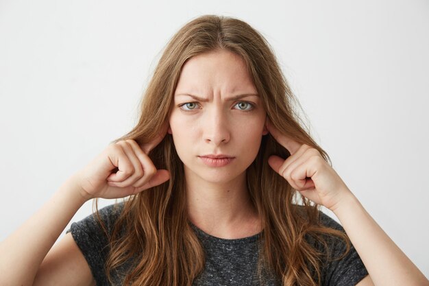 Jeune fille mécontente fermant les oreilles en fronçant les sourcils.