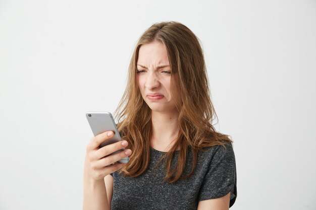 Jeune fille mécontente mécontente en regardant l'écran du téléphone.