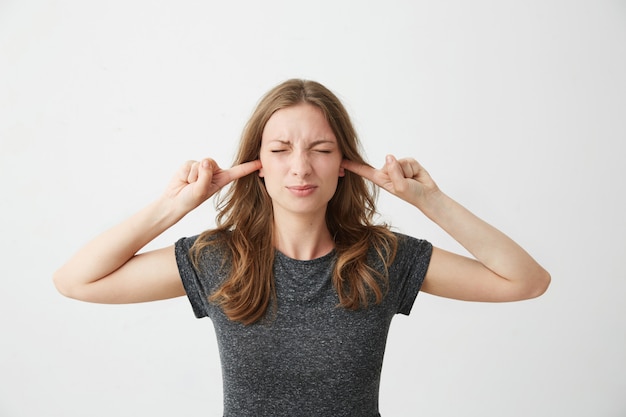 Jeune fille mécontente, les yeux fermés fermant les oreilles en fronçant les sourcils.