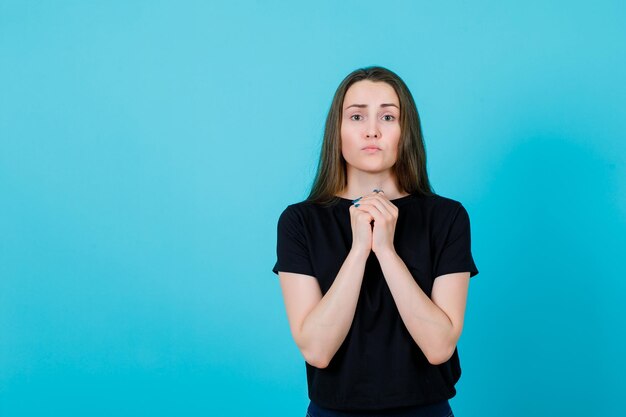 Jeune fille mendie en se tenant la main sur la poitrine sur fond bleu