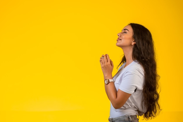 Jeune fille met ses mains sous son menton et prie sur fond jaune.