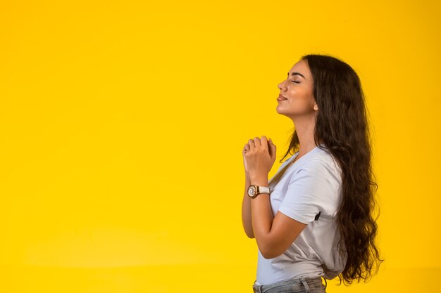 Jeune fille met ses mains sous son menton et prie, vue de profil.