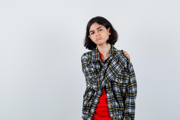 Jeune fille mettant la main sur l'épaule en chemise à carreaux et t-shirt rouge et l'air mignon, vue de face.