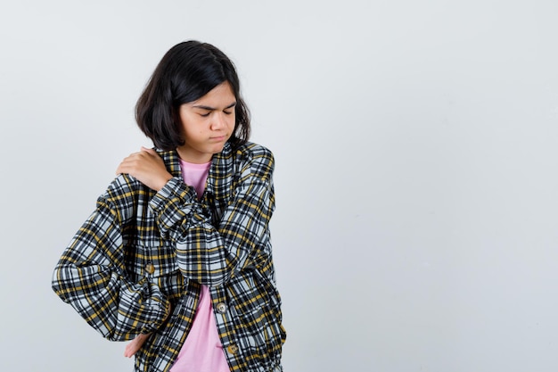 Jeune fille mettant une main sur l'épaule tout en tenant une autre main sur la taille en chemise à carreaux et t-shirt rose et l'air épuisé, vue de face.