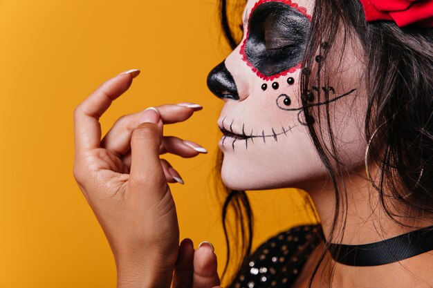 Jeune fille mexicaine avec des roses dans ses cheveux et l'art en forme de crâne sur le visage pose mignon avec ses yeux fermés