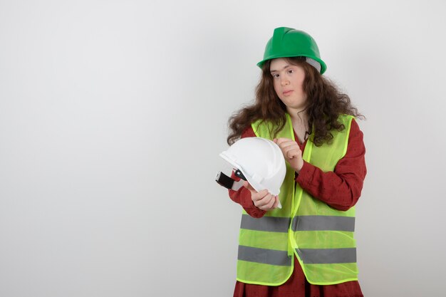 jeune fille mignonne avec le syndrome de Down debout dans un gilet et tenant des casques de protection.