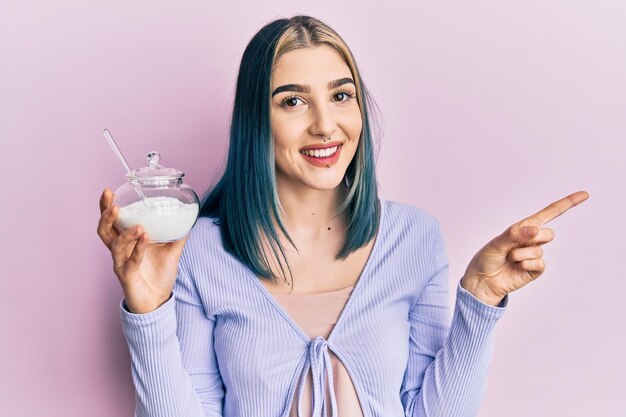 Jeune fille moderne tenant un bol avec du sucre souriant heureux pointant avec la main et le doigt sur le côté