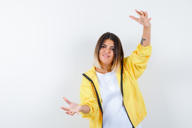 Jeune fille montrant des échelles en t-shirt blanc, veste jaune et à la vue de face, confiant.