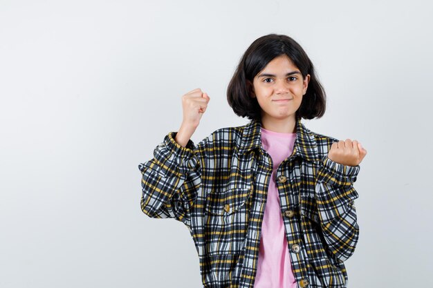 Jeune fille montrant le geste du gagnant en chemise à carreaux et t-shirt rose et semblant mignonne