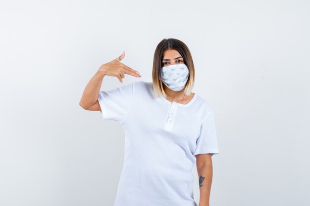 Jeune fille montrant le geste du pistolet en t-shirt blanc, masque et à la confiance. vue de face.