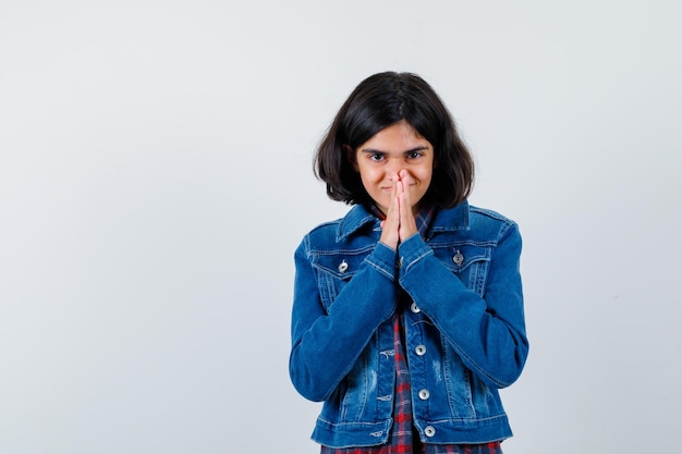 Jeune fille montrant le geste de namaste en chemise à carreaux et veste en jean et à la recherche de sérieux