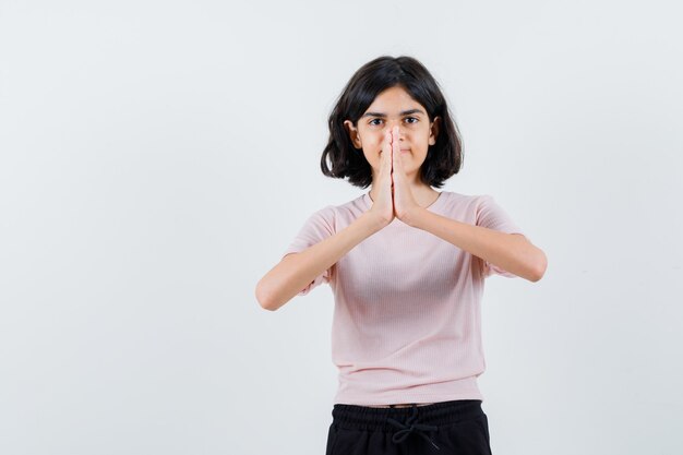 Jeune fille montrant le geste de namaste en t-shirt rose et pantalon noir et à heureux