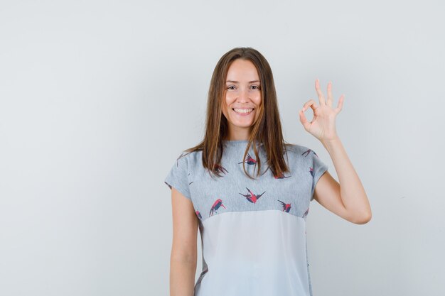 Jeune fille montrant le geste ok en t-shirt et à la joyeuse. vue de face.