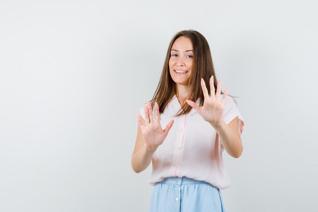 Jeune fille montrant le geste de refus en t-shirt, jupe et à l'optimiste, vue de face.