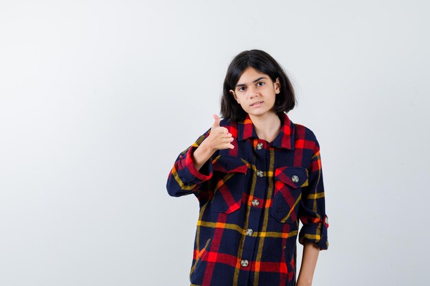 Jeune fille montrant le pouce en chemise à carreaux et l'air heureux. vue de face.