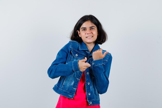 Jeune Fille Montrant Les Pouces Vers Le Haut Avec Les Deux Mains En T-shirt Rouge Et Veste En Jean Et L'air Heureux. Vue De Face.