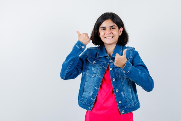 Jeune Fille Montrant Les Pouces Vers Le Haut Avec Les Deux Mains En T-shirt Rouge Et Veste En Jean Et L'air Heureux. Vue De Face.