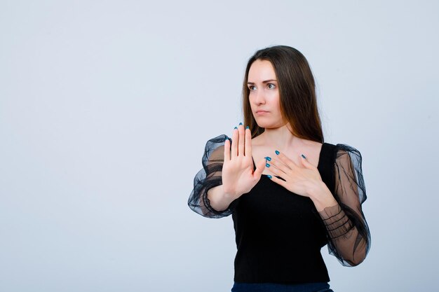 La jeune fille montre le geste d'arrêt en regardant loin sur le fond blanc