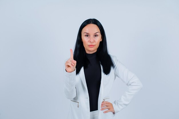 La jeune fille montre un geste minute et met l'autre main sur la taille sur le fond blanc