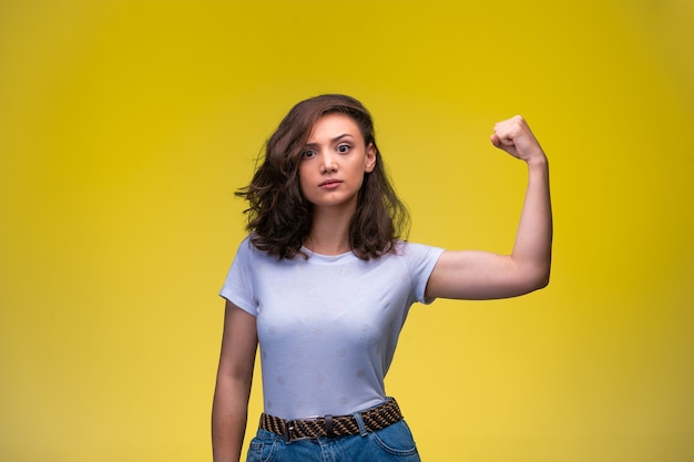 Jeune fille montre ses muscles dans un bras et fait un visage agressif.