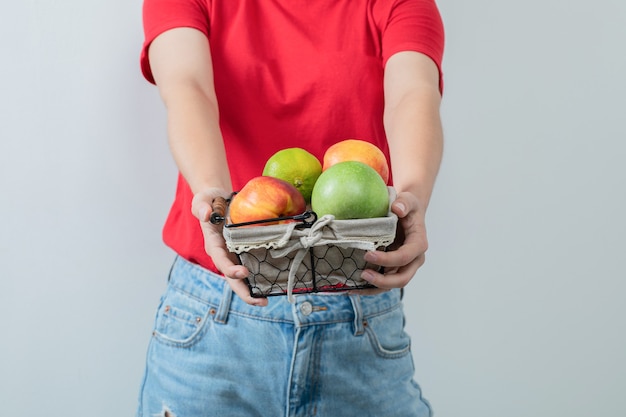 Jeune fille offrant une corbeille de fruits à la main.