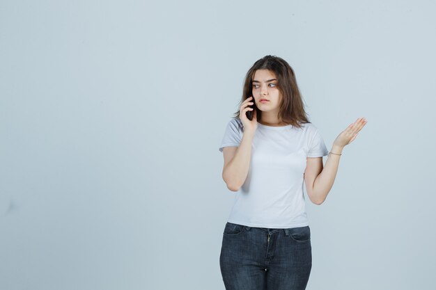 Jeune fille parlant au téléphone mobile en t-shirt, jeans et à la recherche de sérieux. vue de face.