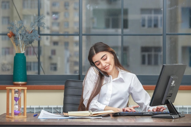 Jeune fille parlant au téléphone tout en travaillant sur le pc