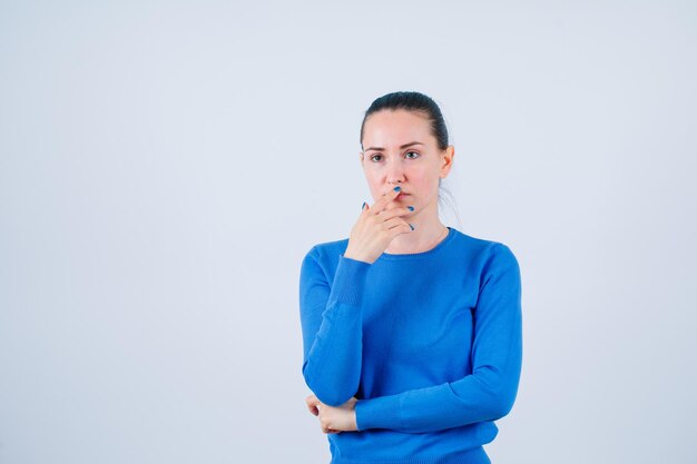 Jeune fille pense en mettant la main sur la bouche sur fond blanc