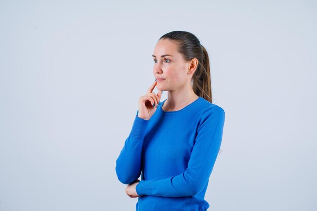 Jeune fille pense en tenant l'index sur les lèvres sur fond blanc